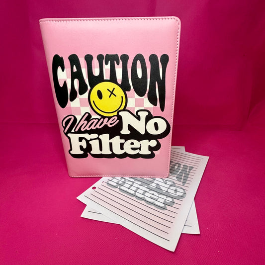 Baby pink A5 faux leather binder with 'Caution I Have No Filter' in drippy black lettering and a yellow x-eye smiley on a checkered pink background
