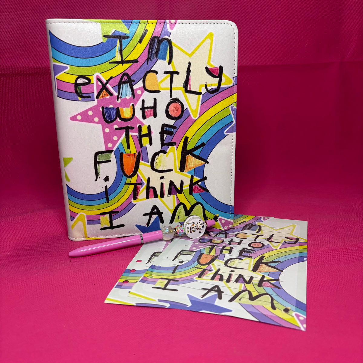 Full-bleed A5 faux leather binder with 'I'm exactly who the fuck I think I am' in raw black block letters over a rainbow star-burst background