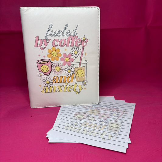 Cream A5 faux leather binder with 'fueled by coffee and anxiety' in pastel retro fonts, surrounded by smiley-faced latte, iced coffee, and daisies