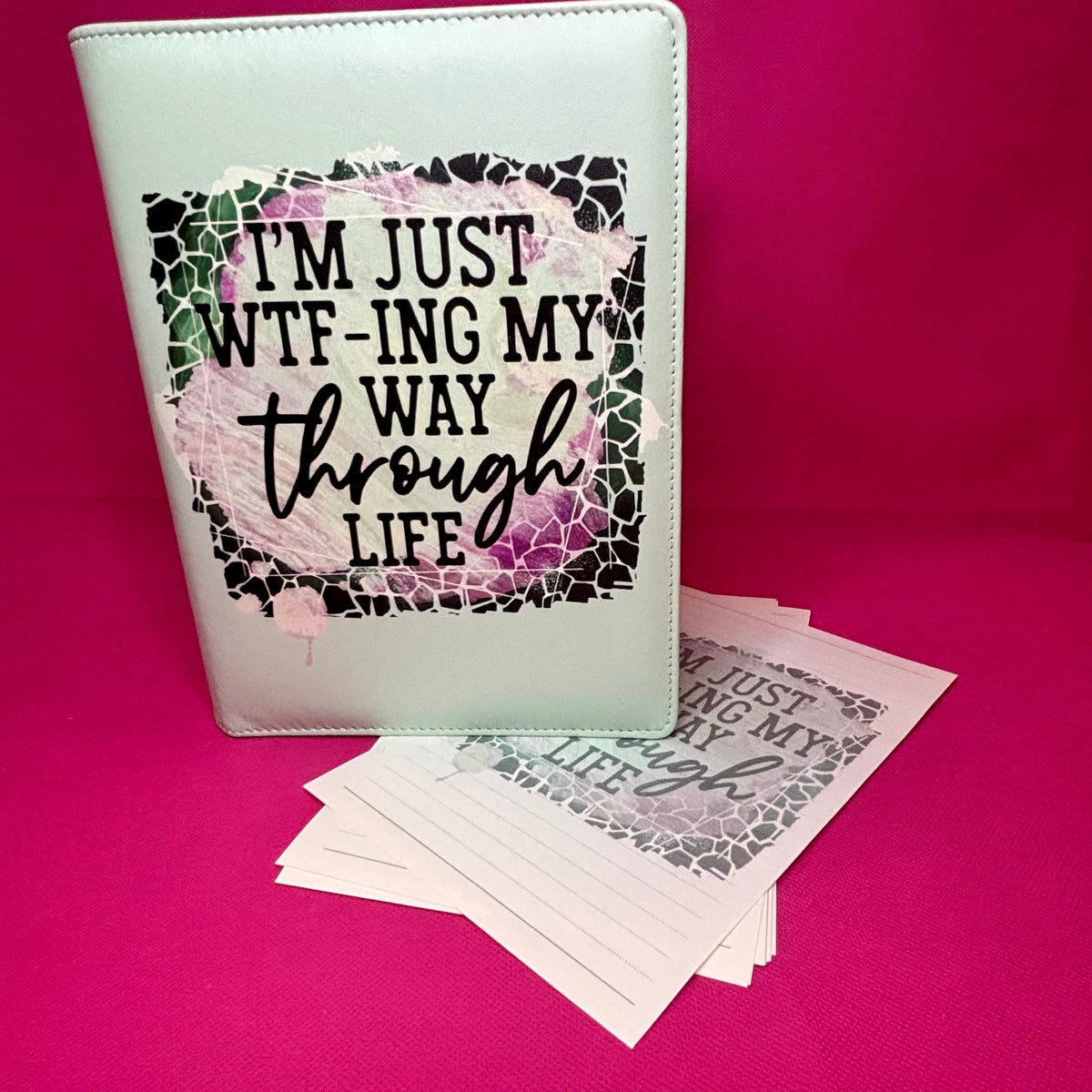 Mint green A5 faux leather binder with 'I'm just WTF-ing my way through life' in a broken-glass frame over a purple-pink watercolor wash