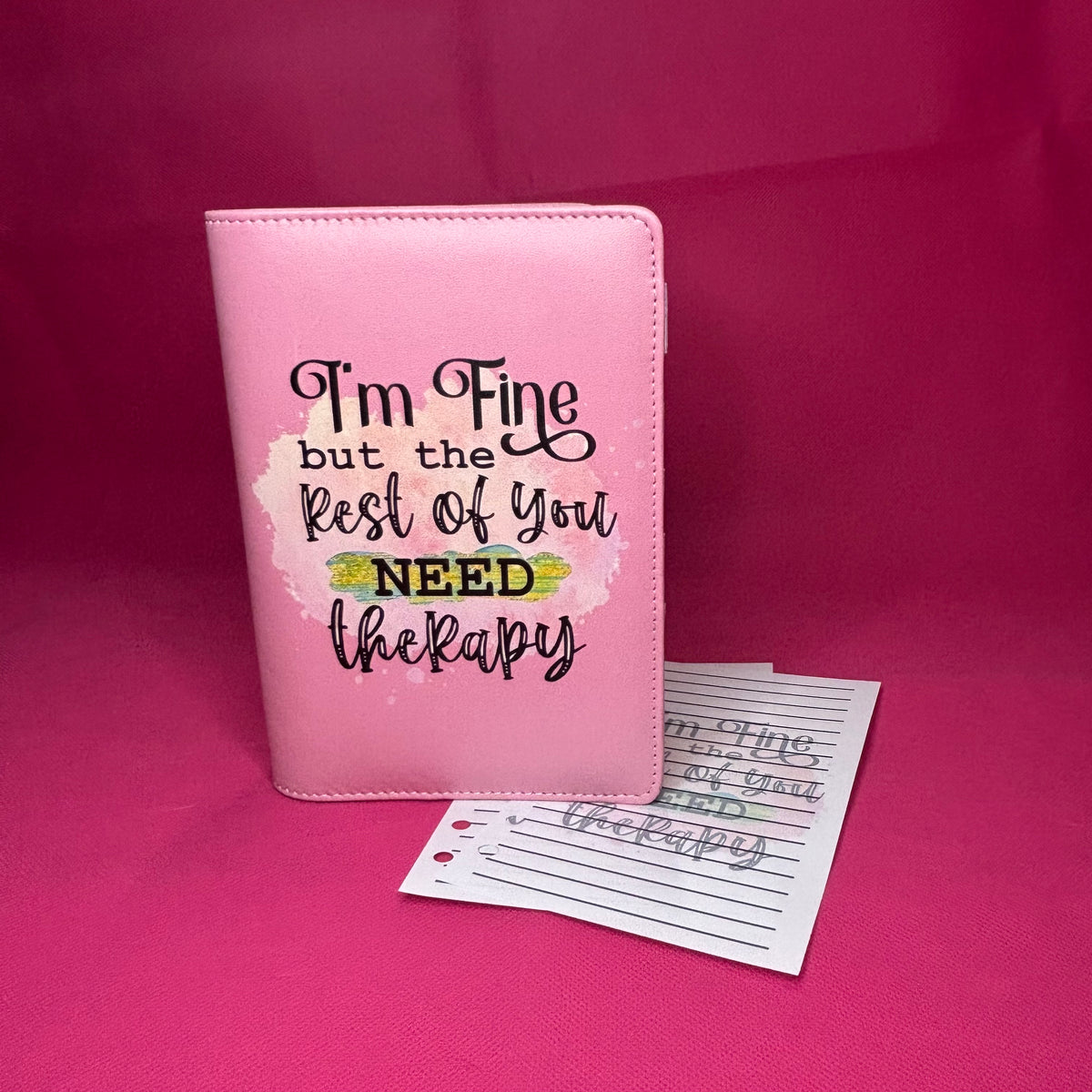 Pink A6 faux leather binder with 'I'm Fine but the Rest of You NEED therapy' in black hand-lettered script on a pastel watercolor splash