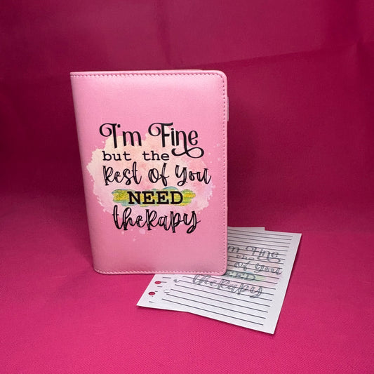 Pink A6 faux leather binder with 'I'm Fine but the Rest of You NEED therapy' in black hand-lettered script on a pastel watercolor splash