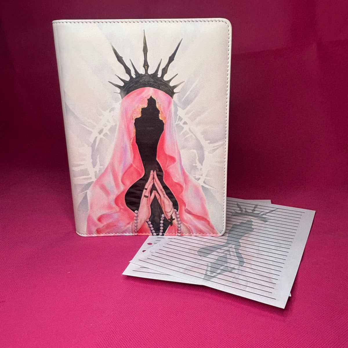 Pearl white A5 faux leather binder with a spike-crowned veiled figure in pink mantle, praying hands with rosary, and a crown of thorns silhouette behind